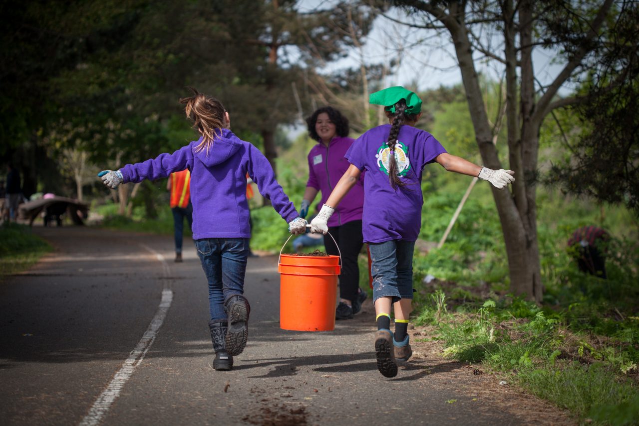 Two youth carrying a bucket together on the road