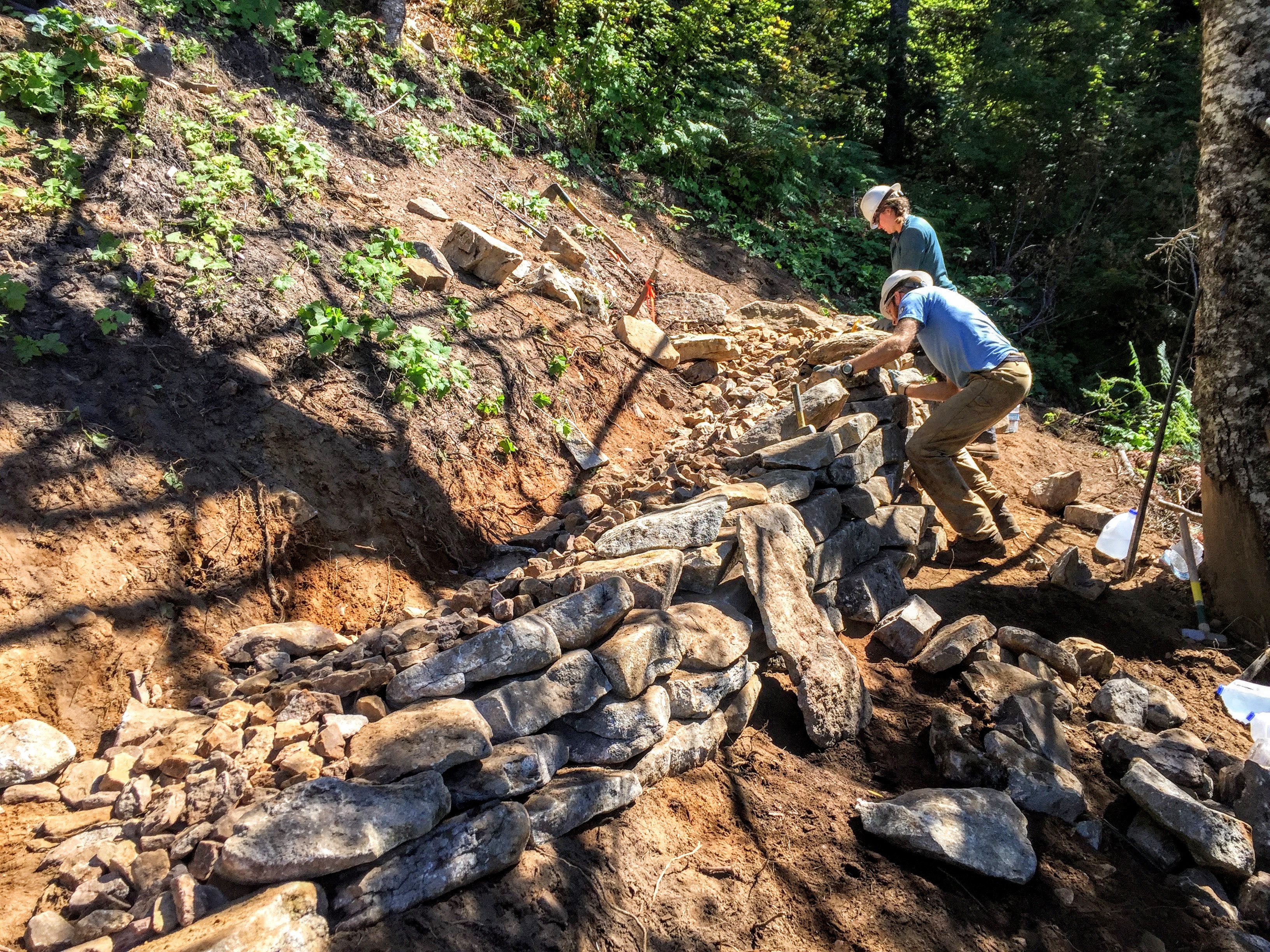 image of two people building a rock wall on a trail